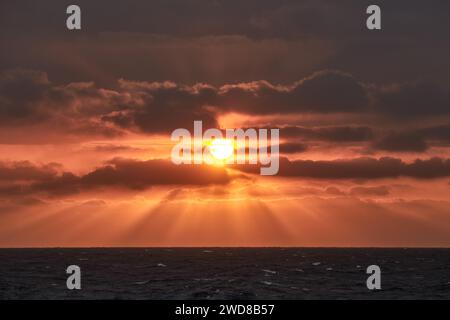 Beautiful red and yellow sunset in the sea with sun in the sky and sun rays shining through the clouds. Stock Photo