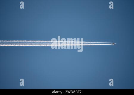 Photo of airplane flying horizontally  in the clear blue sky, leaving vapor trail in the air. Stock Photo