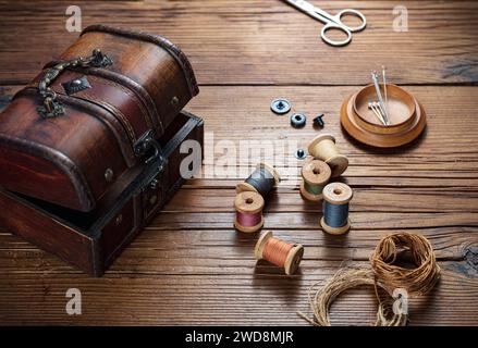 sewing thread with needles and a trunk for accessories on a wooden table Stock Photo