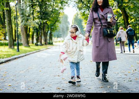 Disabled child is walking in the outdoor park like other people. Little girl has a young mom to take care of closely, Life in the education age of Stock Photo