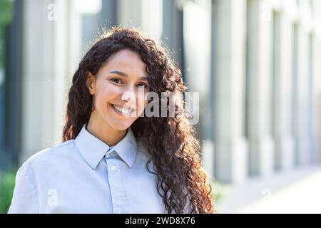 Portrait of a confident and successful young Latin American woman with curly hair outside a city office building. Stock Photo