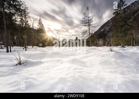 Sun shining through clouds behind snowy landscape Stock Photo