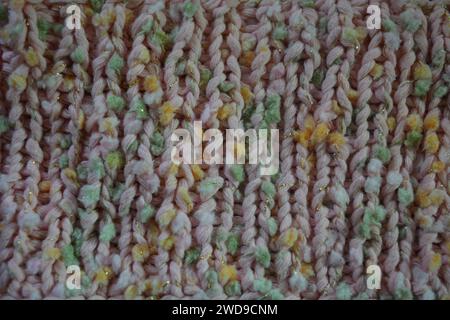 Hand weaving, knitting. A beautiful patterned background is knitted from pink threads with colored inserts. Stock Photo