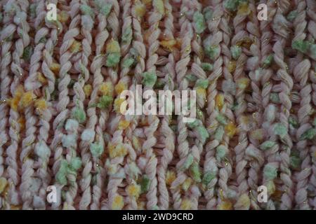 Hand weaving, knitting. A beautiful patterned background is knitted from pink threads with colored inserts. Stock Photo