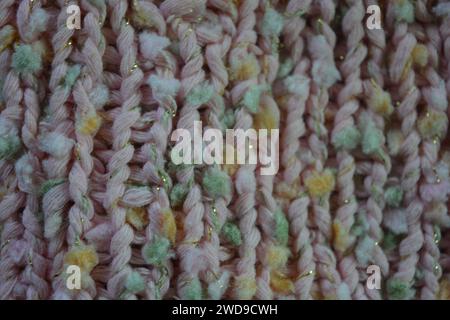 Hand weaving, knitting. A beautiful patterned background is knitted from pink threads with colored inserts. Stock Photo