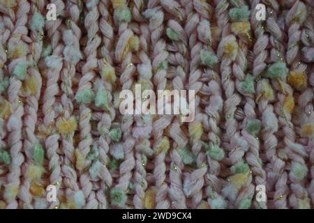 Hand weaving, knitting. A beautiful patterned background is knitted from pink threads with colored inserts. Stock Photo
