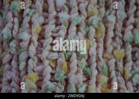 Hand weaving, knitting. A beautiful patterned background is knitted from pink threads with colored inserts. Stock Photo