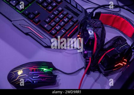 View of professional gaming peripherals including a Bloody (A4Tech) mouse, a mechanical keyboard, and a headset with red accents at an esports tournament. The background shows a high-end PC case with glowing RGB fans, creating a vivid atmosphere in a gaming lounge Stock Photo