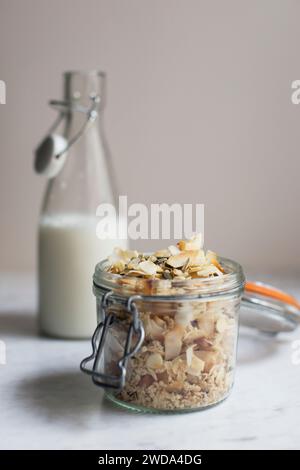 Homemade granola with coconut flakes, seeds and oats in glass jar, almond milk bottle in background, healthy breakfast concept. Stock Photo