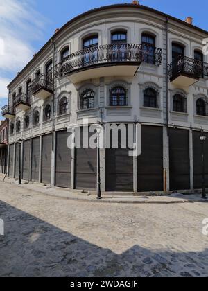 257 White-gray, Neoclassical corner house at the cobbled Rrugica Alush Koprencka and Rrugica Petraq Nasi corner, Old Bazaar area. Korca-Albania. Stock Photo