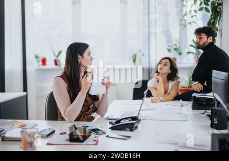 Engaged female employee sharing ideas in a bright office while colleagues listen attentively Stock Photo