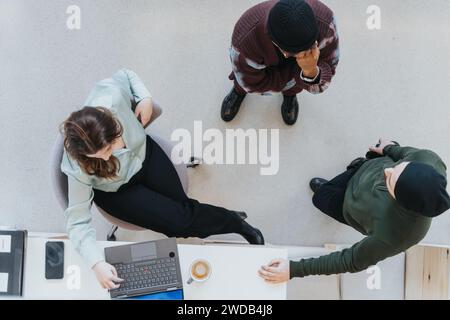 Top view of three colleagues having a casual business meeting with laptop and coffee. Stock Photo