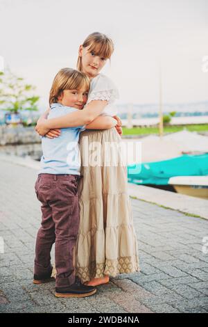 Outdoor portrait of two adorable kids hugging each other, little boy and girl spending time together, vertical image Stock Photo