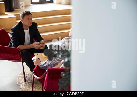 Handsome young man sitting in armchair holding smartphone in hands Stock Photo