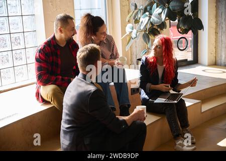 Colleagues team listening to red-haired woman art director who holding laptop Stock Photo