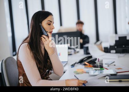 Professional woman multitasking in busy office environment, on phone call with paperwork Stock Photo