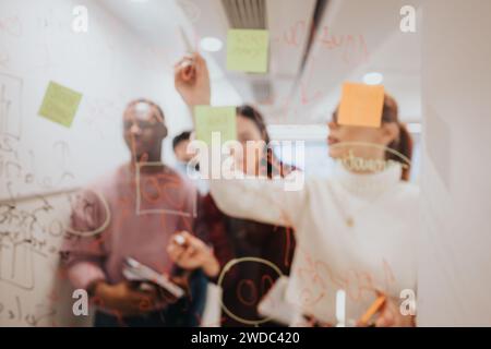 Diverse colleagues brainstorming and strategizing in a pleasant office, using sticky notes on a glass door to create a successful project plan. Stock Photo