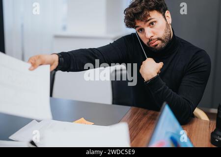 A young male person attentively examines papers, showcasing concentration and dedication in a modern office setting. Stock Photo