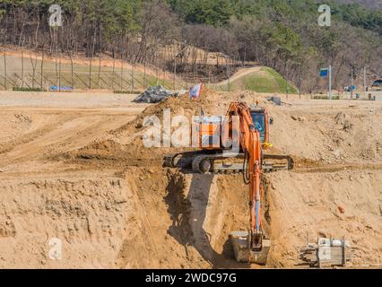 Daejeon, South Korea, March 29, 2020:, Orange backhoe moving dirt to create ditch at rural construction site on sunny spring day, South Korea, South Stock Photo