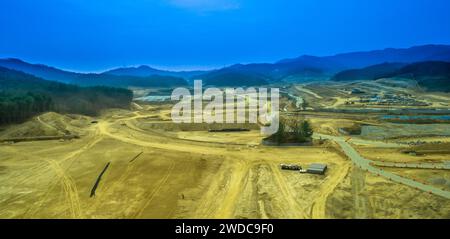 Aerial view of construction site with small cluster of trees fenced off for protection and rolling hills under blue sky in background, South Korea Stock Photo