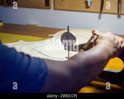 Close up of Stringed instrument maker master luthier hand proceed with graduation work in progress violon cello back plate, using thickness gauge Stock Photo