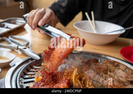 A woman's hand picks up grilled meat marinated in a Korean wok on a grill in a restaurant. Stock Photo