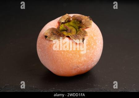 Frozen food. Frozen persimmon covered with frost melting on a black ...
