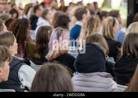 Diverse group of people gathered at an outdoor event, listening attentively to a speaker. Stock Photo