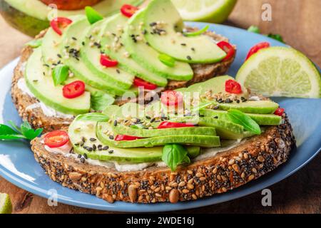 Avocado toast - bread with avocado slices, pieces chilli pepper and black sesame on blue plate closeup. Stock Photo