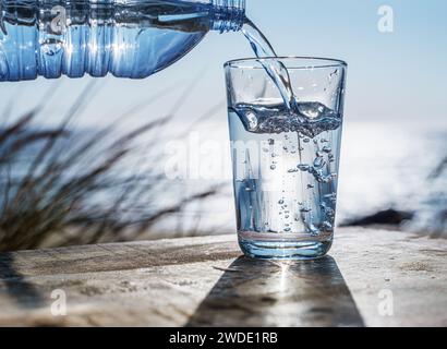 Pouring water into a glass from plastic bottle. Nature background. Stock Photo