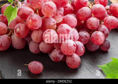 Cluster of red table grape with grape leaves on gray background. Stock Photo