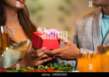 Close up shot, Boyfriend giving surprise gift to girlfriend during candle light dinner - concept of valentines or birthday present and couple Stock Photo