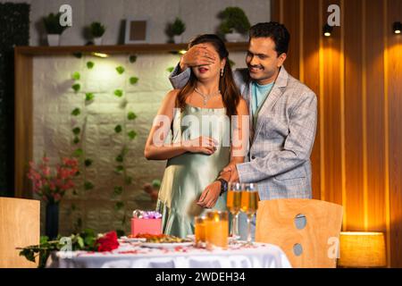 happy man giving surprise candlelight dinner to wife or girlfriend at restaurant for valentines day - concept of excitement, anniversary present and Stock Photo