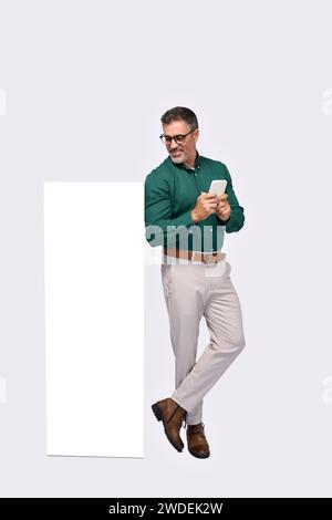 Happy older business man standing near big phone mockup using smartphone. Stock Photo
