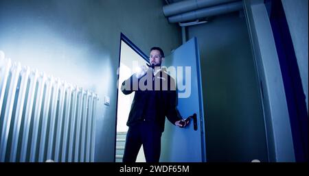 Mature Male Security Guard With Flashlight Standing In Corridor Of The Building Stock Photo