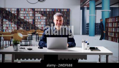 Reading On Laptop In Library. Academic Education Stock Photo