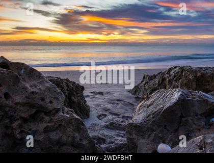 Early morning beach with a captivating sunrise over textured rocks and sandy terrain, ideal for travel themes and serene home decor. Stock Photo