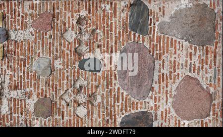 Abstract background from a wall with bricks and stones. Old fortress wall of red brick interspersed with large cobblestones Stock Photo
