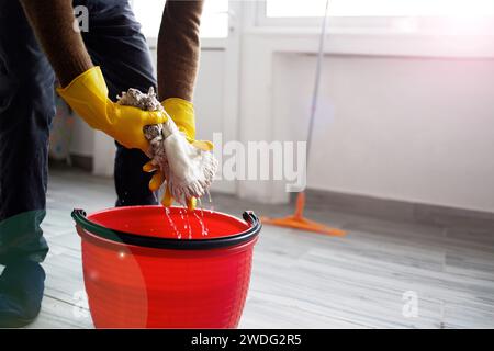 Hands in rubber gloves wring out a mop over a bucket. The concept of cleanliness and health care. Stock Photo