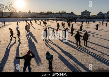 Wintervergnügen auf dem zugefrorenen Nymphenburger Kanal, München, Januar 2024 Deutschland, München, Januar 2024, Wintervergnügen am Nymphenburger Schlosskanal, Eislaufen und Spazierengehen, viele Münchner bummeln am Samstagnachmittag bei Minusgraden über den zugefrorenen Kanal oder laufen Schlittschuh, die tiefstehende Wintersonne wirft lange Schatten und taucht die Szene in ein warmes Gegenlicht, Temperaturen bei -8 Grad und Sonnenschein, Schloss Nymphenburg, Eisfläche noch tragfähig, Wettervorhersage für die nächsten Tage sagt stark steigende Temperaturen voraus, das Eis wird dann schnell b Stock Photo