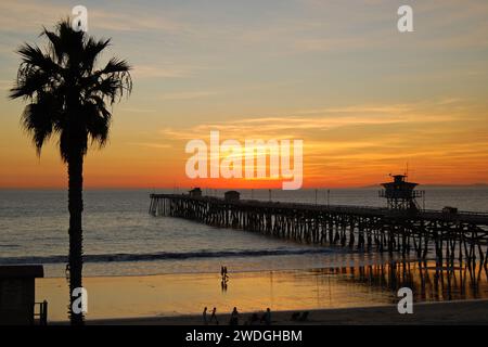 A beautiful sunset develops at the beach and pier in San Clemente, rendering the palm trees and people in silhouette Stock Photo