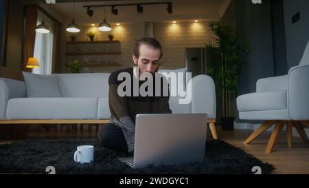 A bearded man sitting on the floor, using laptop computer does remote work Stock Photo