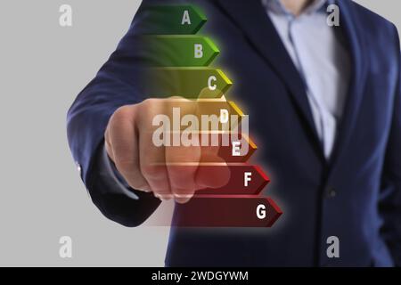 Energy efficiency. Man touching colorful rating on digital screen against light grey background, closeup Stock Photo