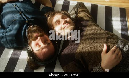 Two young men lying on the floor, wearing headphones, listening to music with eyes closed. Friendship concept Stock Photo