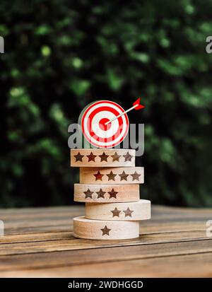 3d goal target icon on top of round wood block stack with one to five stars rating symbols, on green leaves background, vertical style. Business marke Stock Photo