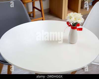 Top view of beautiful blooming white and yellow flowers in ceramic vase ornate with red ribbon decoration on round top wood table with large empty spa Stock Photo