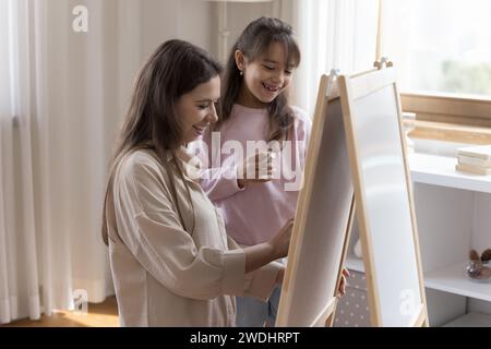 Little daughter and mother drawing on whiteboard with chalks Stock Photo