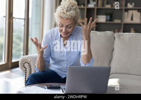Frustrated mature woman calculates expenses, feels annoyed Stock Photo
