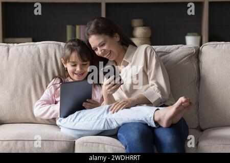 Happy mother and child using modern technologies seated on sofa Stock Photo