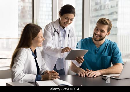 Cheerful diverse clinic medical colleagues in uniforms using tablet computer Stock Photo